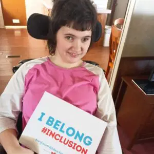 Girl using wheelchair in a pink shirt holding a sign that says I belong #inclusion is a member of the Forget Me Not Friends Club a program of the Forgotten Wishes Foundation