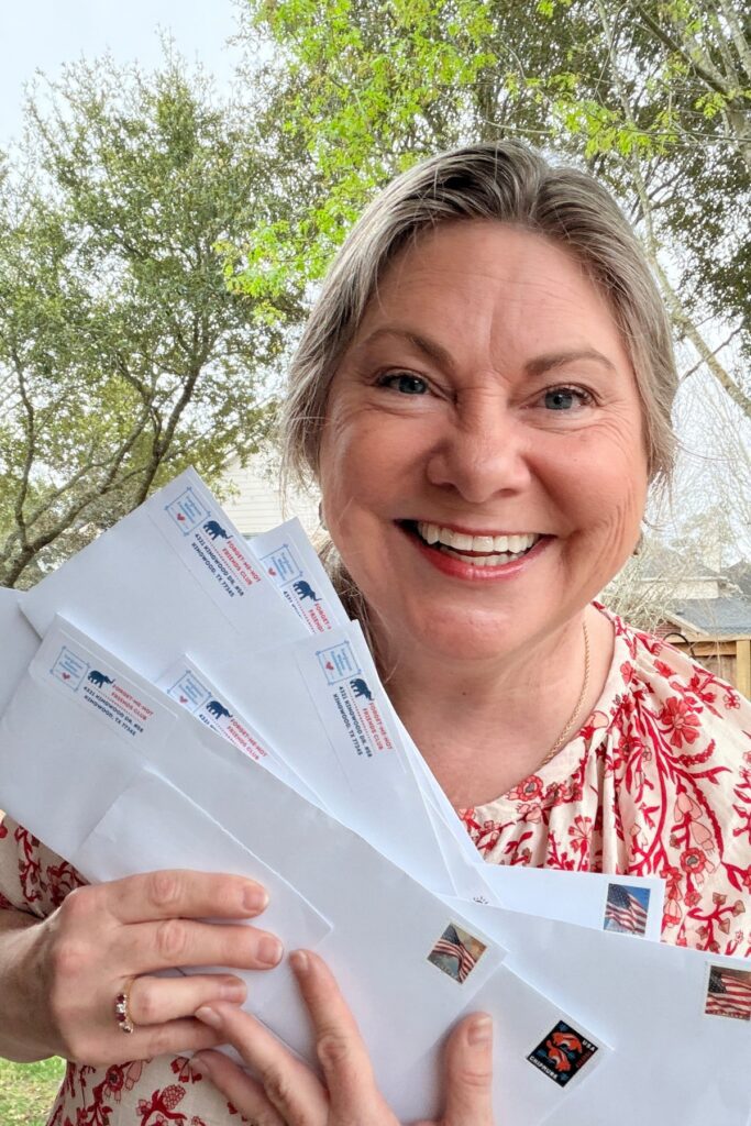 Lisa Dempsey is smiling and holding a batch of letters to be mailed out to Forget-Me-Not Friends Club Members.